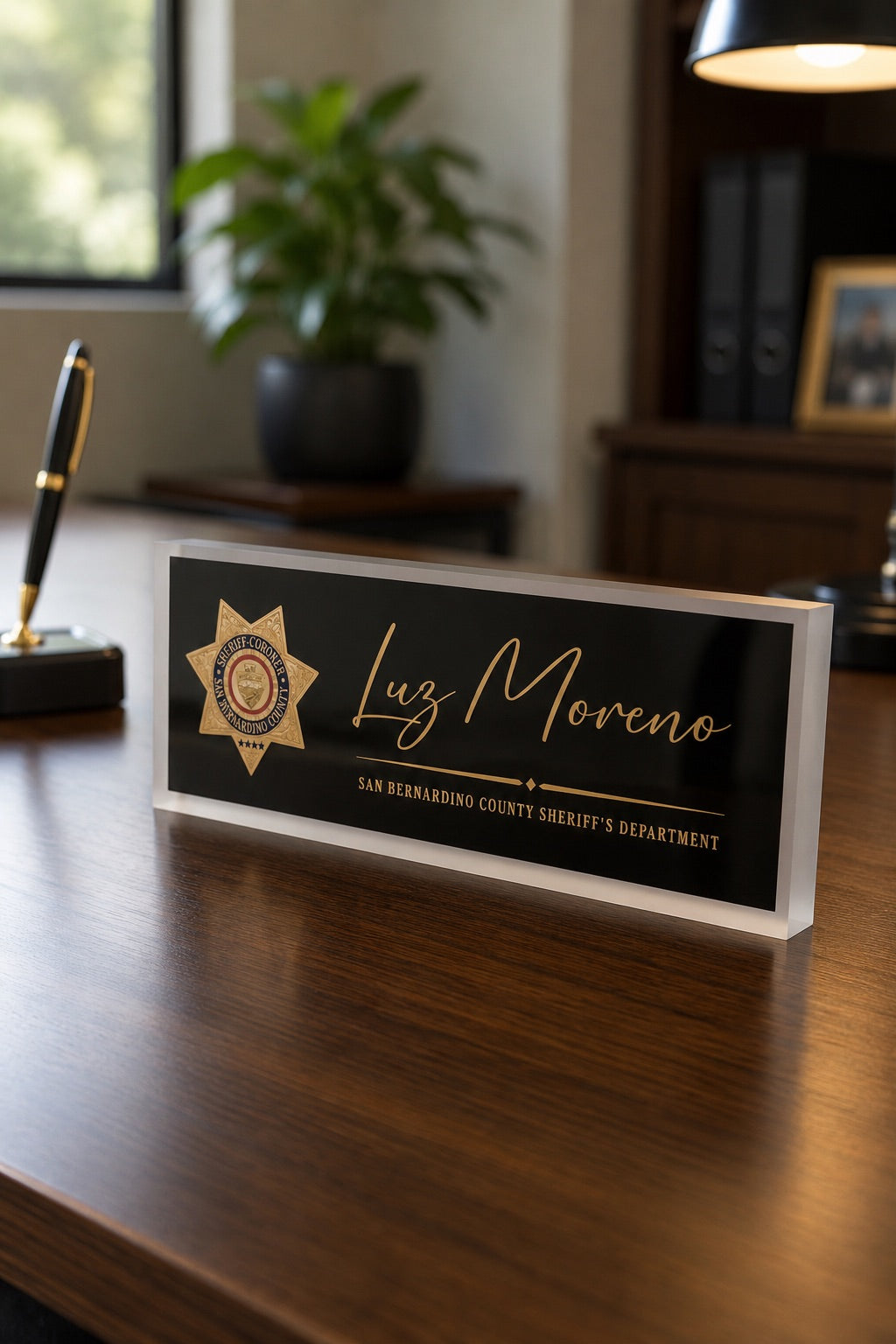 Black and gold personalized acrylic desk nameplate with frosted edges and a sheriff emblem on a wooden desk