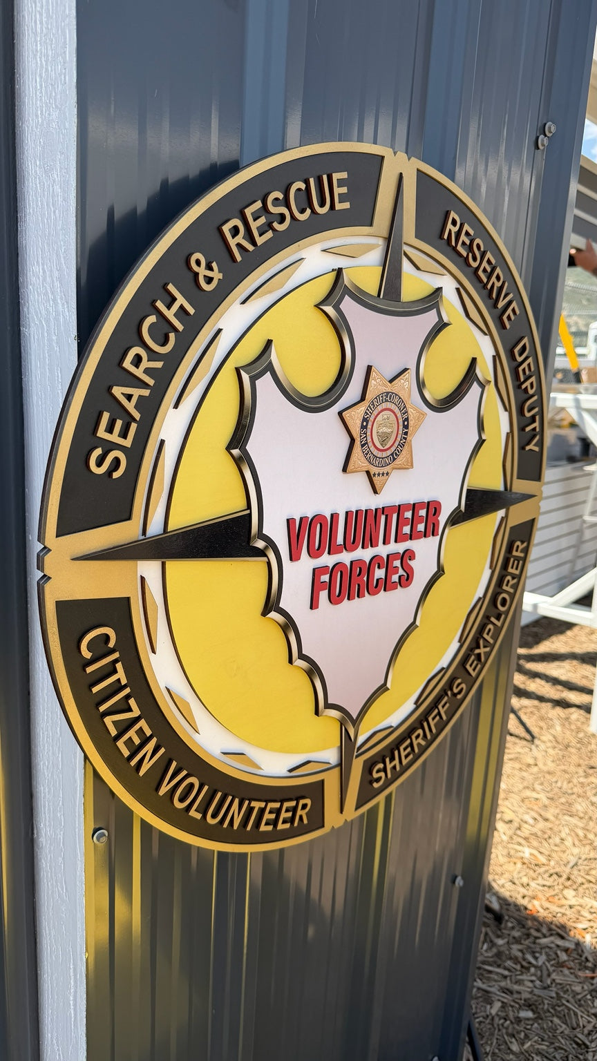 Large layered Volunteer Forces emblem sign with raised lettering and a sheriff star in black, gold, yellow, and red