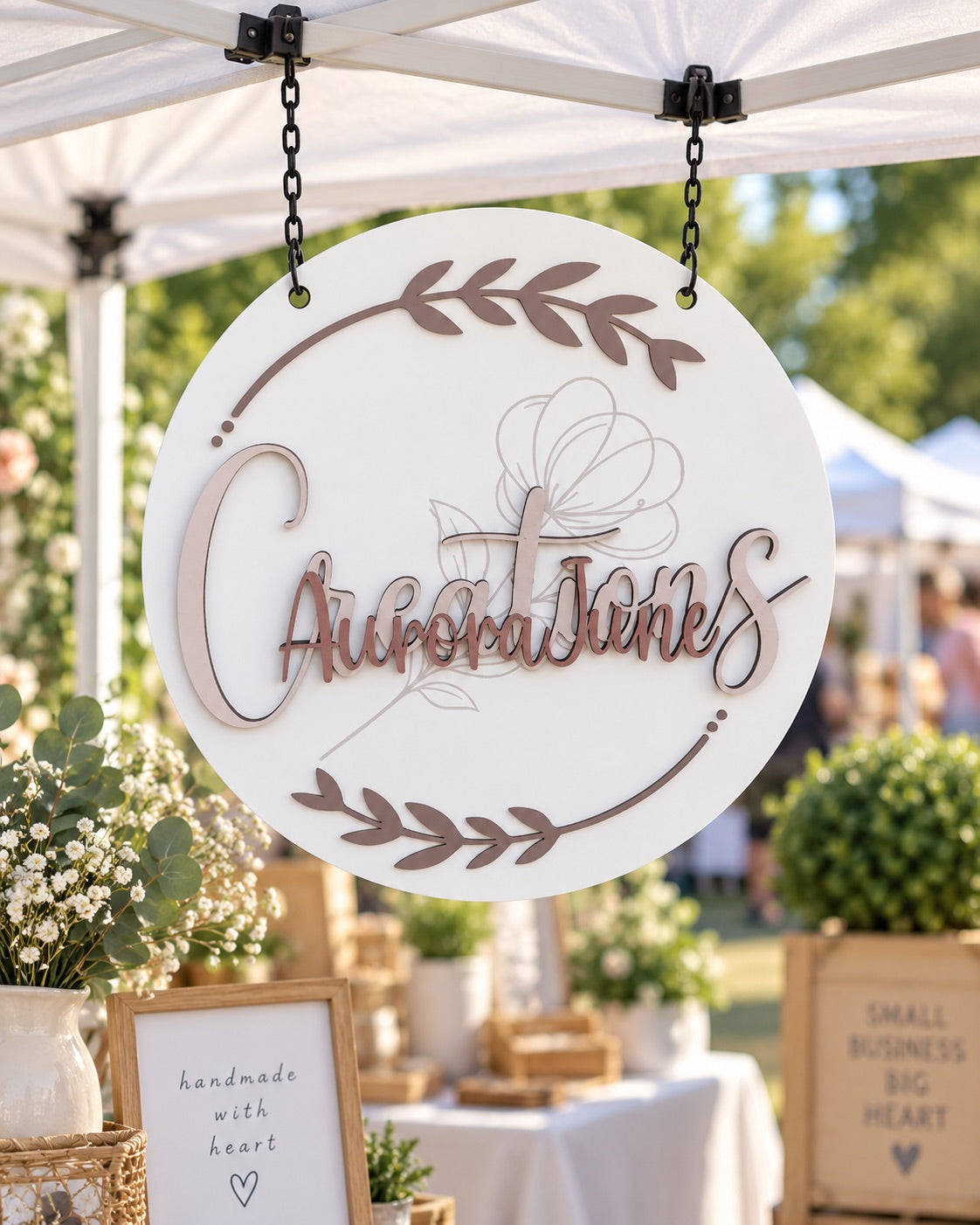 Round Aurora June Creations business sign with raised lettering and botanical details hanging from a canopy